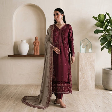 A woman models a traditional Indian salwar kameez suit in deep maroon with matching embroidery, paired with a beige dupatta featuring maroon border detailing, in a warm, neutral-toned room.